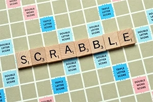 Ξύλινα γράμματα σχηματίζουν τη λέξη SCRABBLE πάνω σε ταμπλό με χρωματιστά τετράγωνα