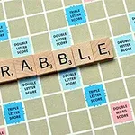 Ξύλινα γράμματα σχηματίζουν τη λέξη SCRABBLE πάνω σε ταμπλό με χρωματιστά τετράγωνα